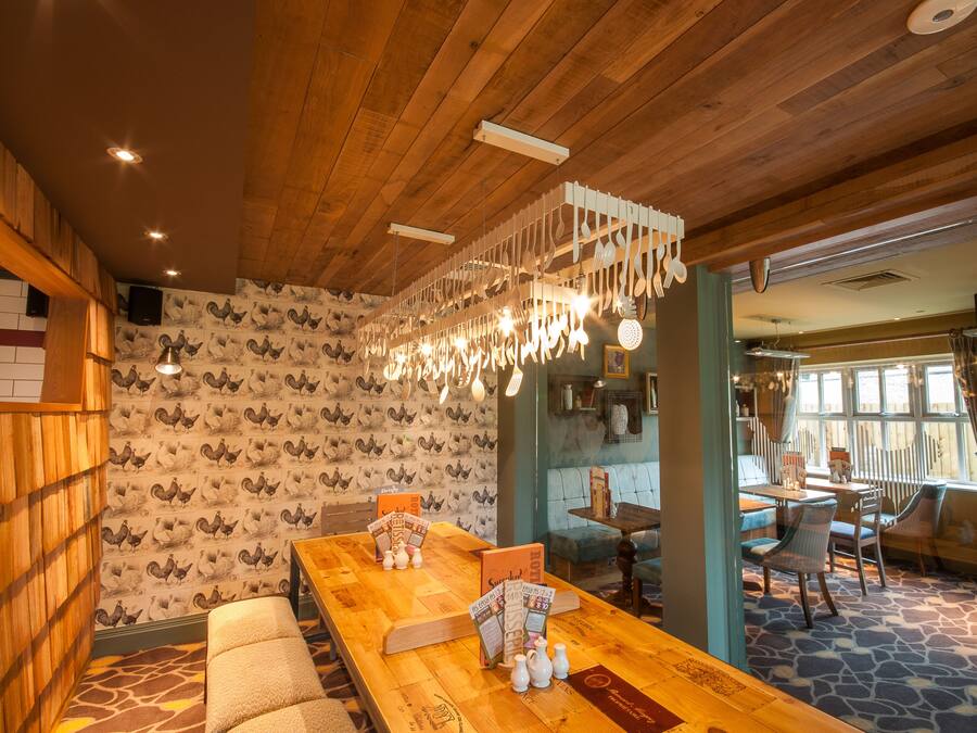 A restaurant interior with wooden ceiling, patterned wallpaper, and a long wooden table with menu stands.