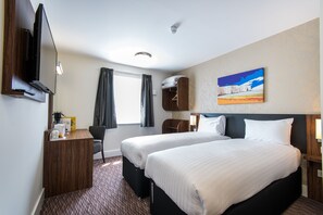 A hotel room with two beds, a desk with a flat-screen TV, a chair, a coat rack, and a painting on the wall. - Canterbury Bell, Margate by Marston's Inns (Broadstairs)