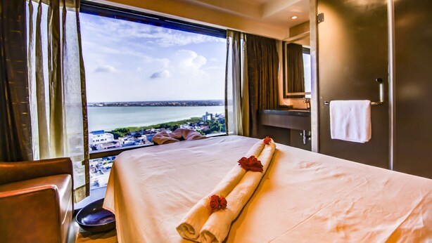 Habitación de hotel con una cama, vista a un cuerpo de agua y un paisaje urbano.