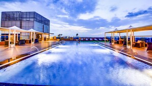 Una piscina en la azotea con áreas de descanso, un edificio moderno y vistas de la ciudad.