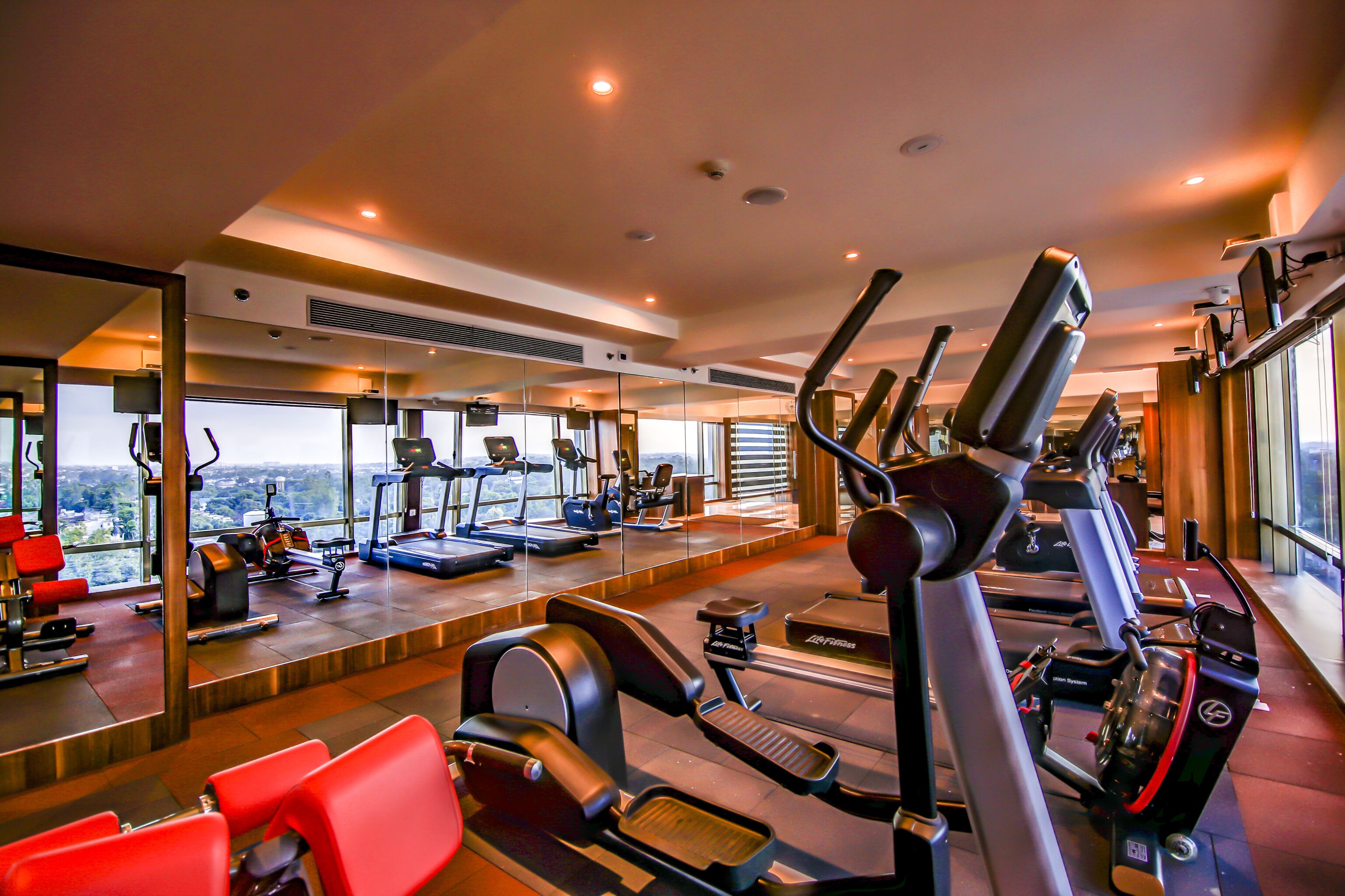 Ein Fitnessstudio mit verschiedenen Trainingsgeräten, einem großen Spiegel und Blick auf die Stadt.