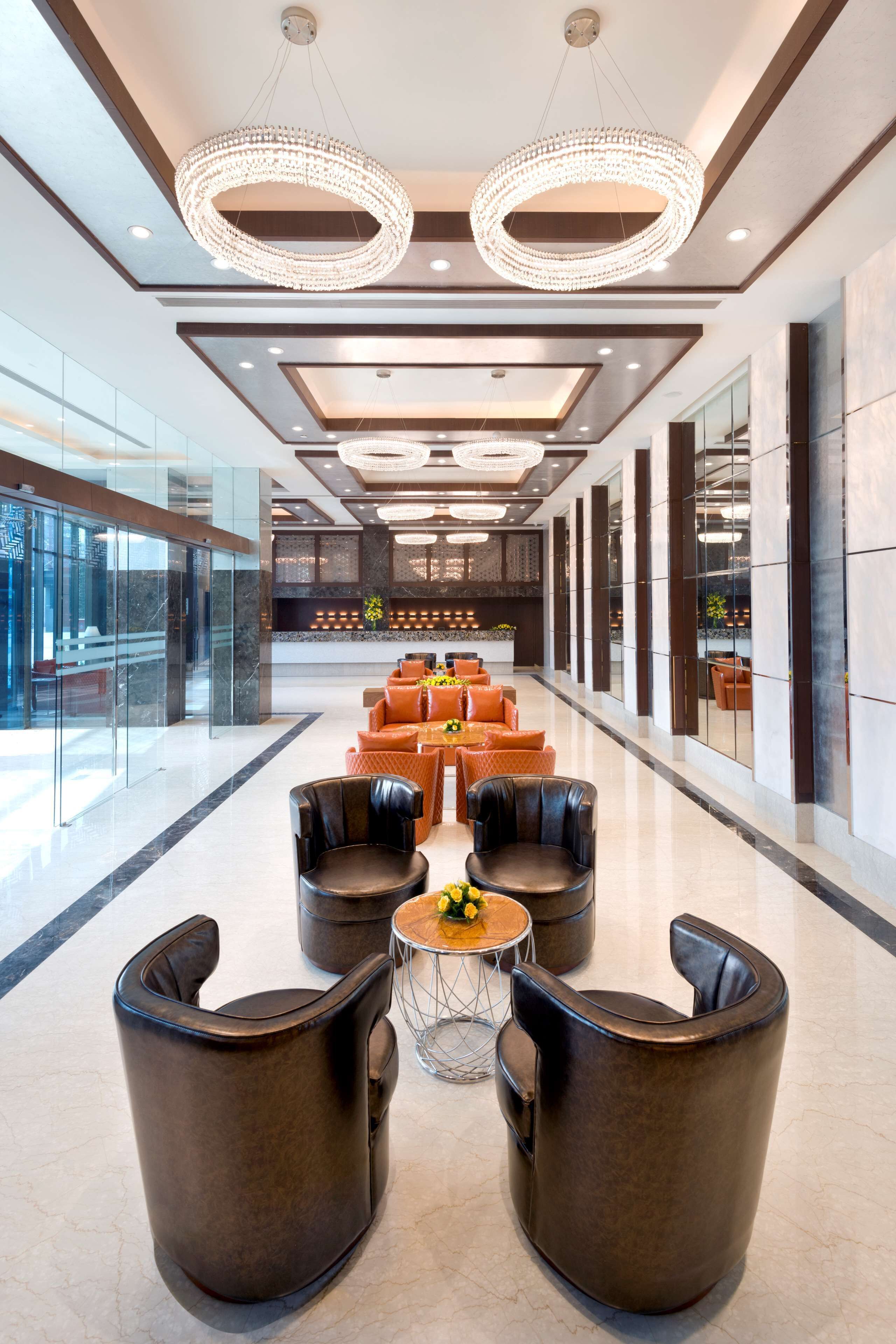 A modern lobby with leather seating, a central round table, and a chandelier.