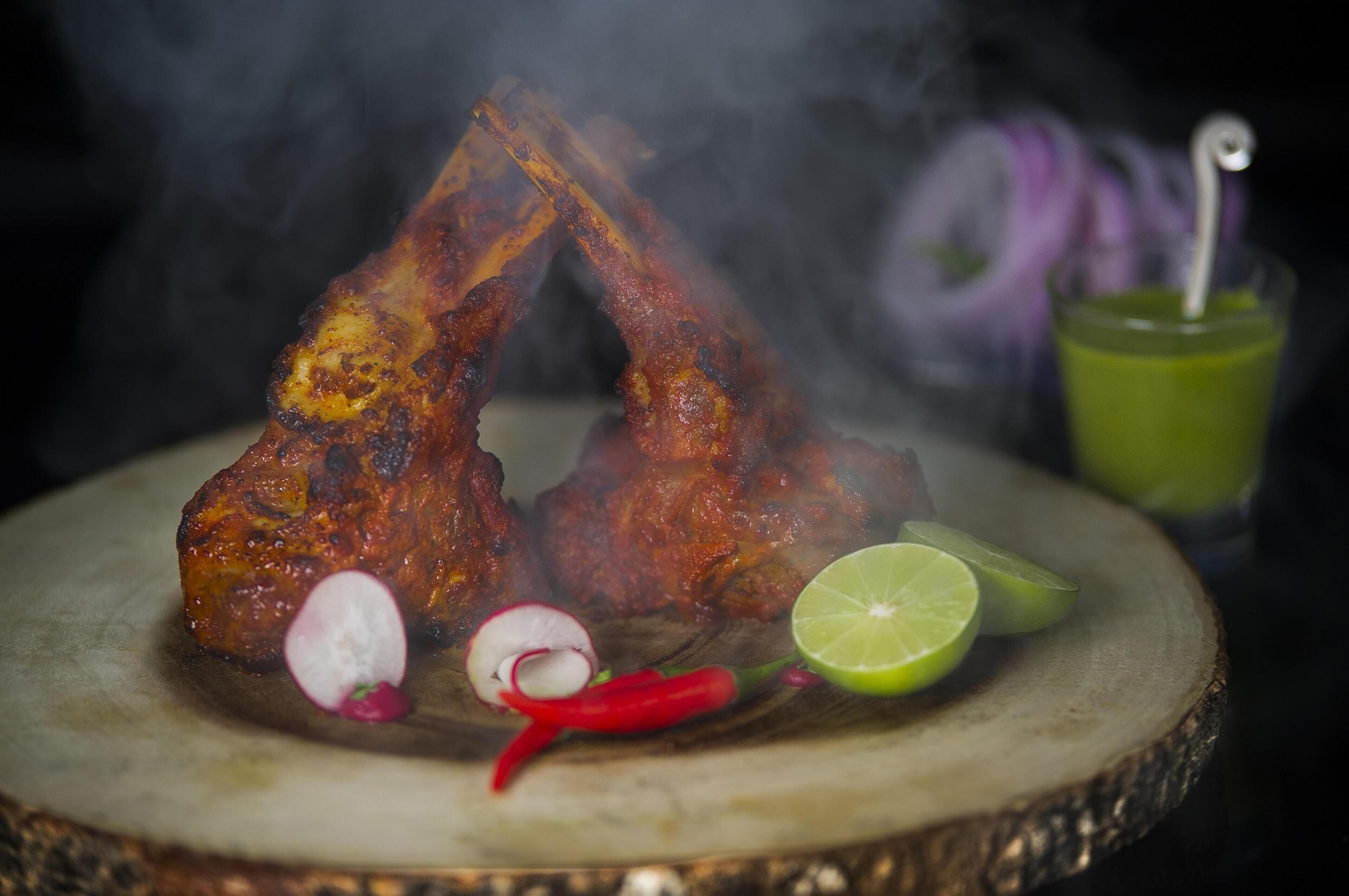 A plate of grilled meat with lime and radish garnish, accompanied by a green drink.