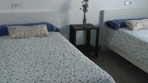 A hotel room with two beds, a small table with a vase, and a painting on the wall. - Chocolate, March (Martos)