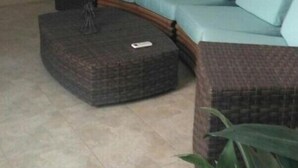 A living room with a light blue sofa, a dark wicker ottoman, a staircase, and a wall-mounted guitar. - Chocolate, March (Martos)