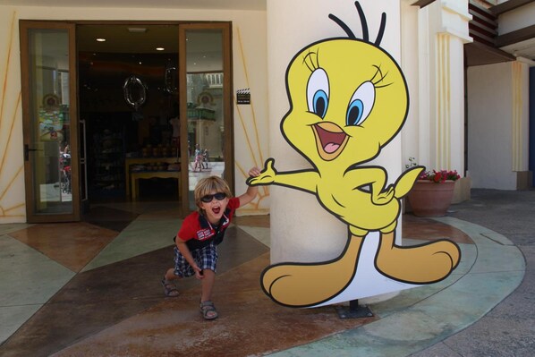 A child interacting with a large cartoon character statue outside a building with glass doors and a tiled floor.