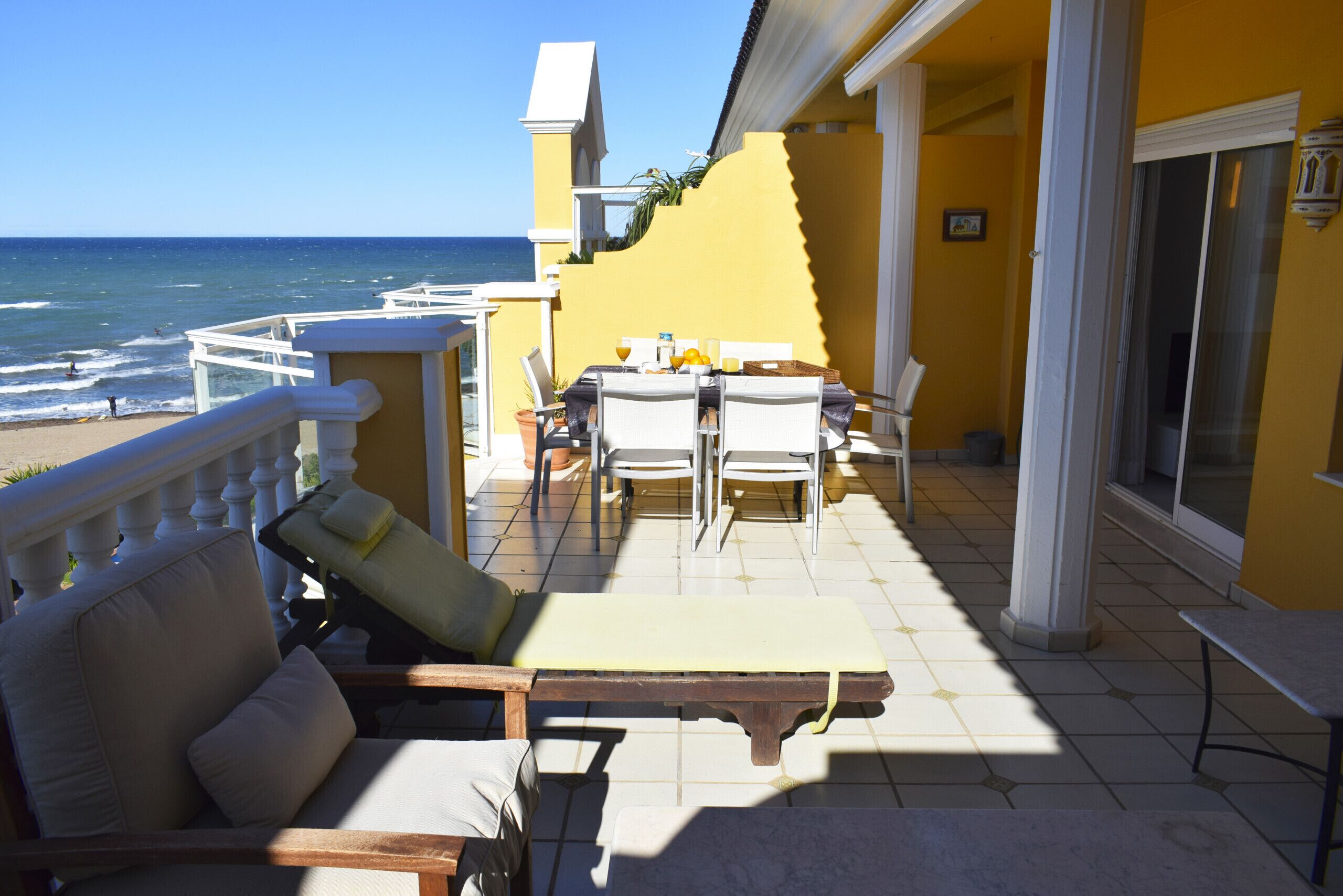 A balcony with a view of the ocean, a table with chairs, and a sofa.