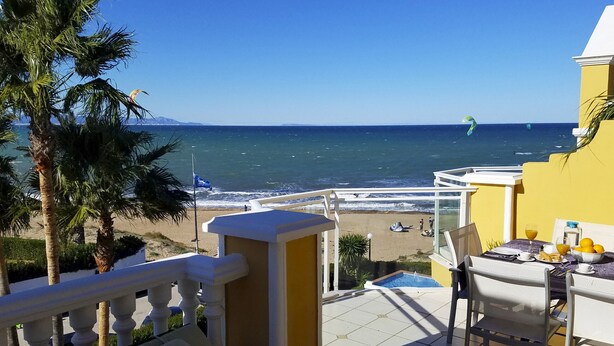 Un balcon avec vue sur la plage, une piscine et une table où sont disposés des aliments pour le petit-déjeuner.