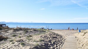 Une plage de sable avec une promenade en bois menant à l’eau, des parasols et un poste de surveillance pour les sauveteurs.
