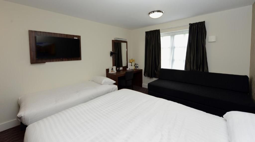A hotel room with two beds, a flat-screen TV, a desk with a mirror, and a window with curtains.