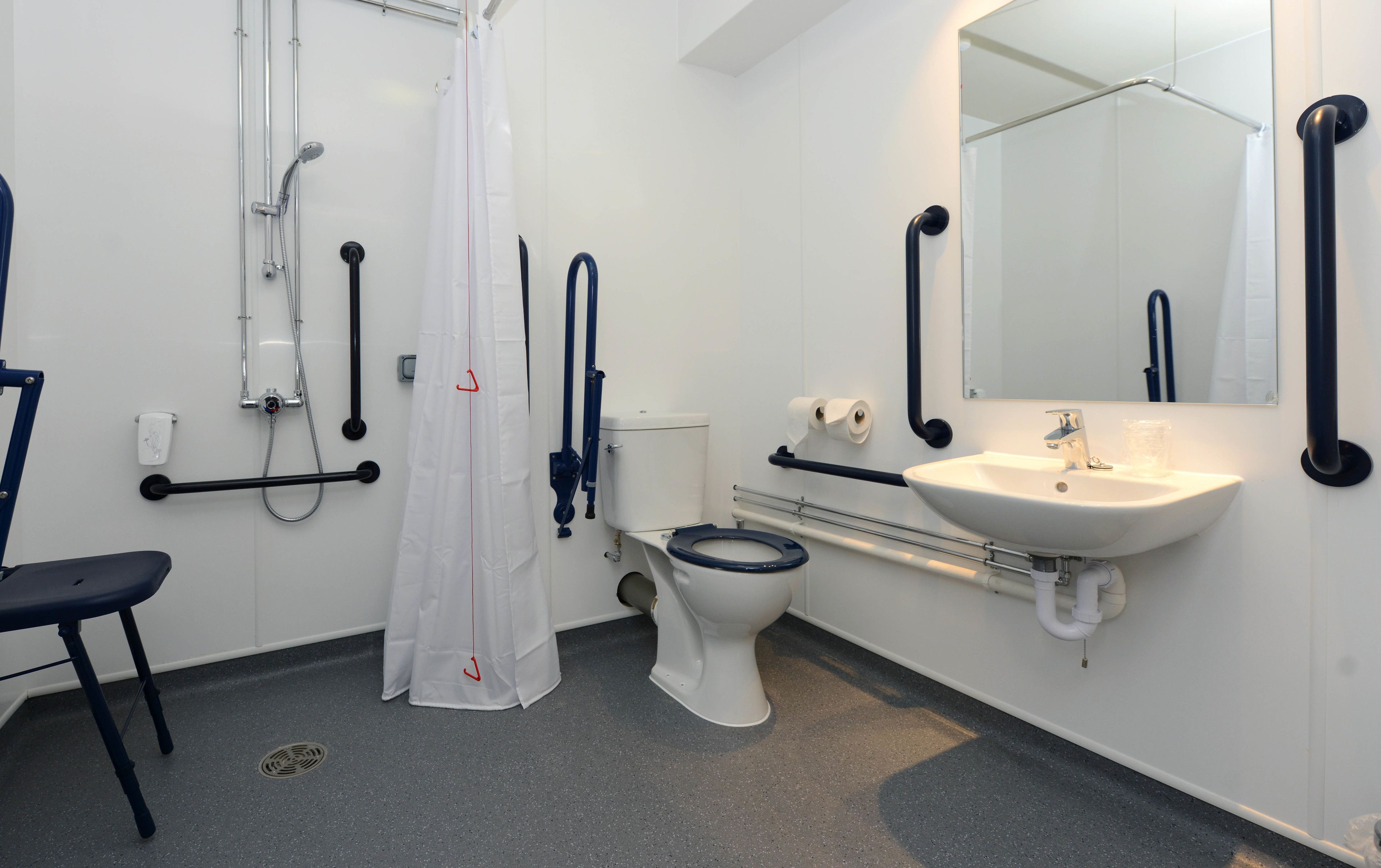 A bathroom with a white toilet, a sink, a shower with a curtain, and grab bars.