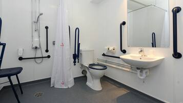 A bathroom with a white toilet, a sink, a shower with a curtain, and grab bars.