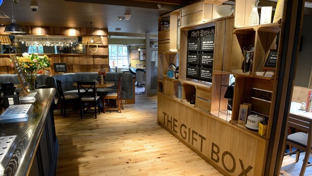A cozy restaurant interior with wooden flooring, a counter labeled 'THE GIFT BOX', and a seating area with tables and chairs. - Fallow Field, Telford by Marston's Inns (Telford)