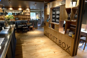 A cozy restaurant interior with wooden flooring, a counter labeled 'THE GIFT BOX', and a seating area with tables and chairs. - Fallow Field, Telford by Marston's Inns (Telford)