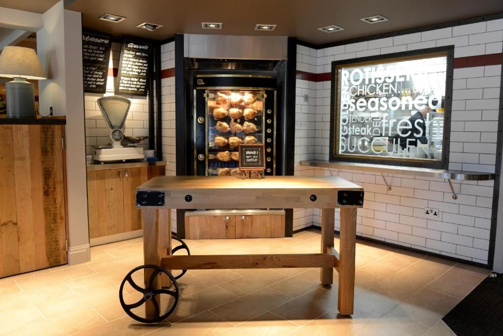 A kitchen area with a wooden table, a bread display case, and a window with a view of the street.
