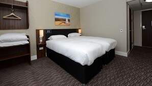 A hotel room with a large bed, a wooden nightstand, a wall-mounted light, a painting, and a door. - Fallow Field, Telford by Marston's Inns (Telford)