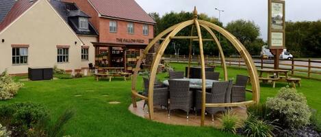 A pub named 'The Fallow Field' with outdoor seating and a wooden pergola structure.
