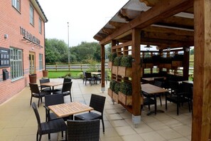 An outdoor patio area with tables and chairs, a wooden pergola, and a brick building labeled 'THE FALLOVER.'