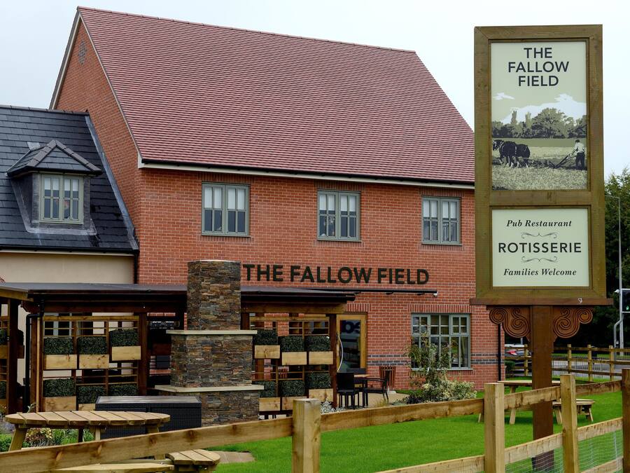 A pub named The Fallow Field with a signboard, brick building, and outdoor seating area.