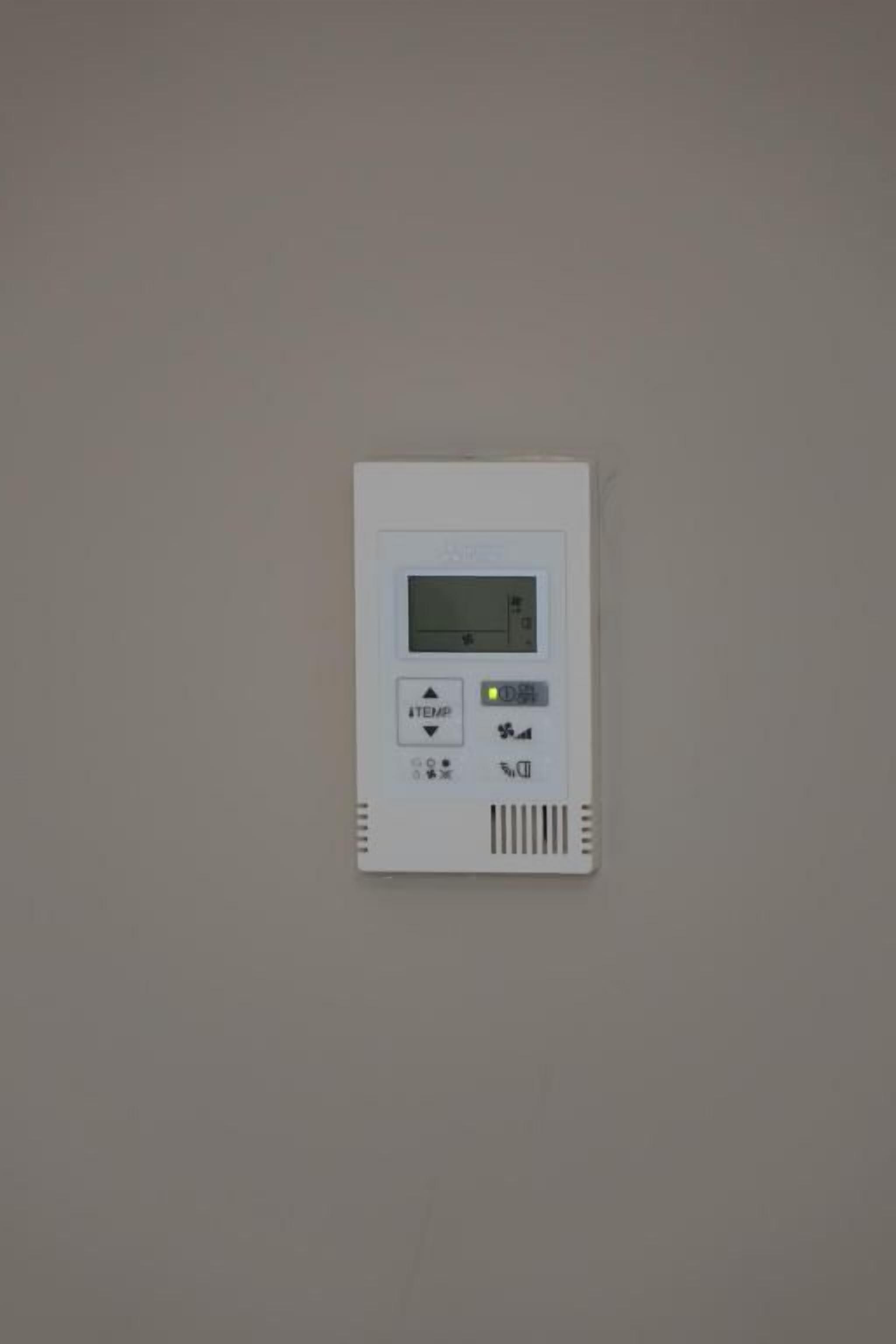 A thermostat mounted on a wall with a digital display, temperature control buttons, and a percentage indicator.
