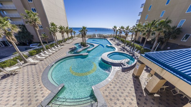 A pool area with multiple swimming pools, lounge chairs, and palm trees. -  Crystal Tower Condos (Gulf Shores)