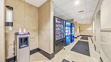 A hotel corridor with vending machines, including a water dispenser and a Pepsi machine, and a tiled floor with black and beige tiles.
