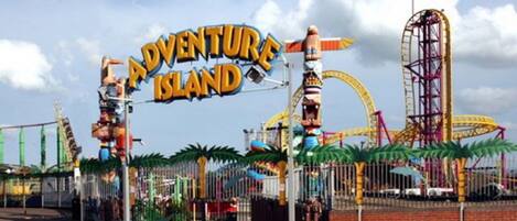 A theme park entrance with a sign reading "Adventure Island" and various amusement rides in the background.