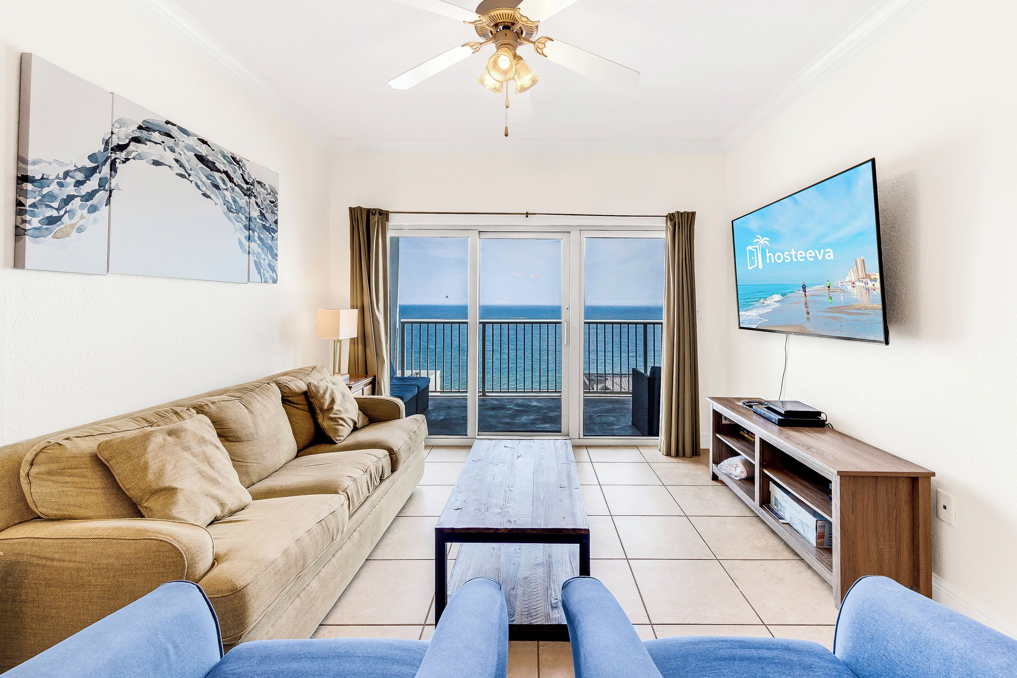 A living room with a sofa, a coffee table, a TV, and a balcony with a view of the sea.