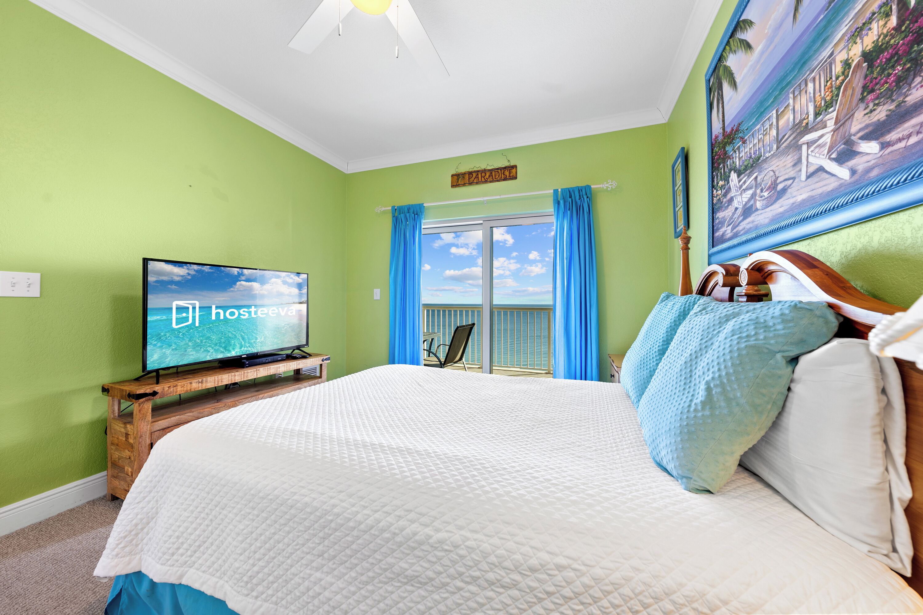 A bedroom with a bed, a television on a wooden stand, a window with curtains, and a painting on the wall.