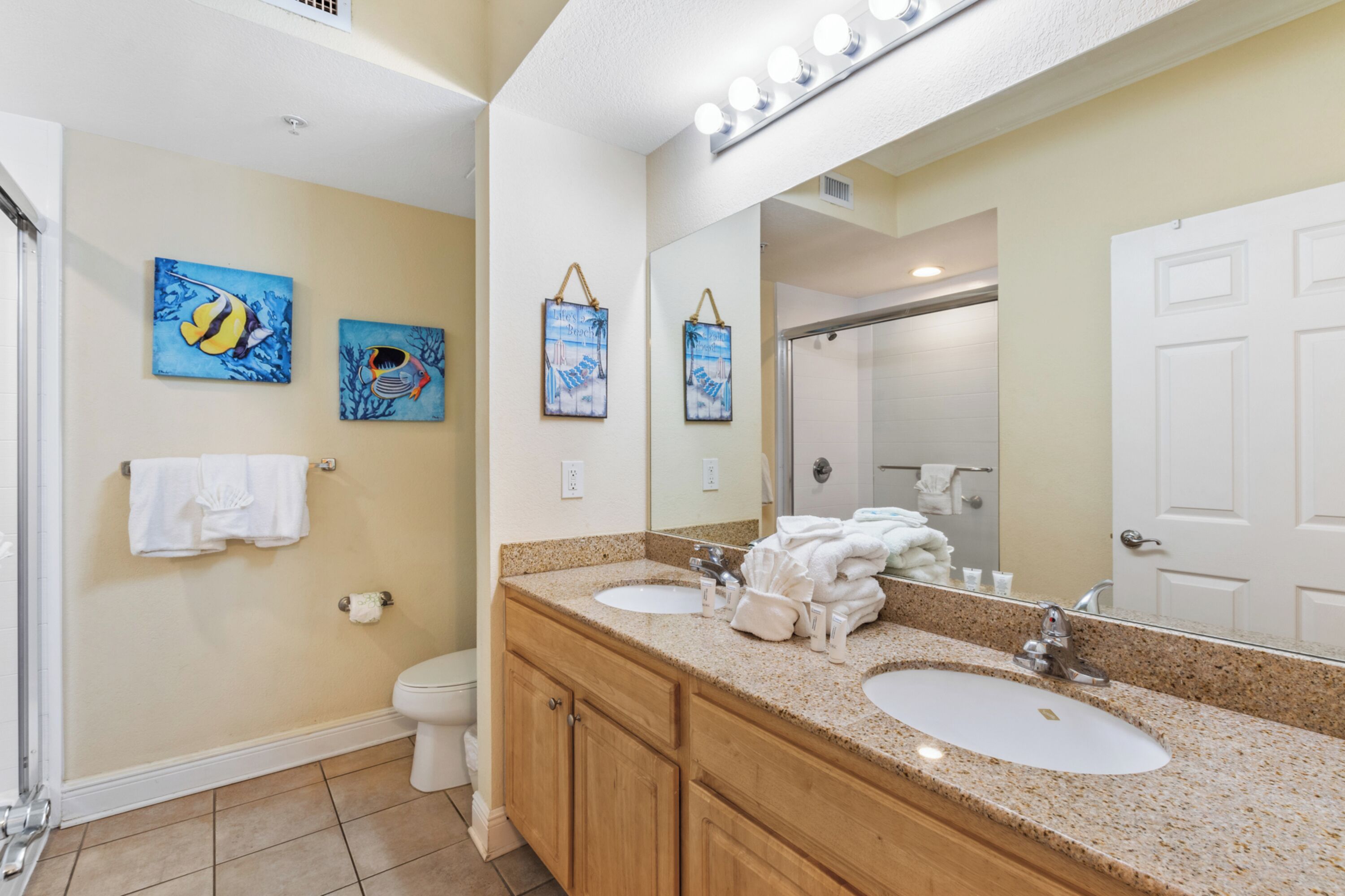 A bathroom with two sinks, wooden cabinets, a large mirror, and artwork on the wall.