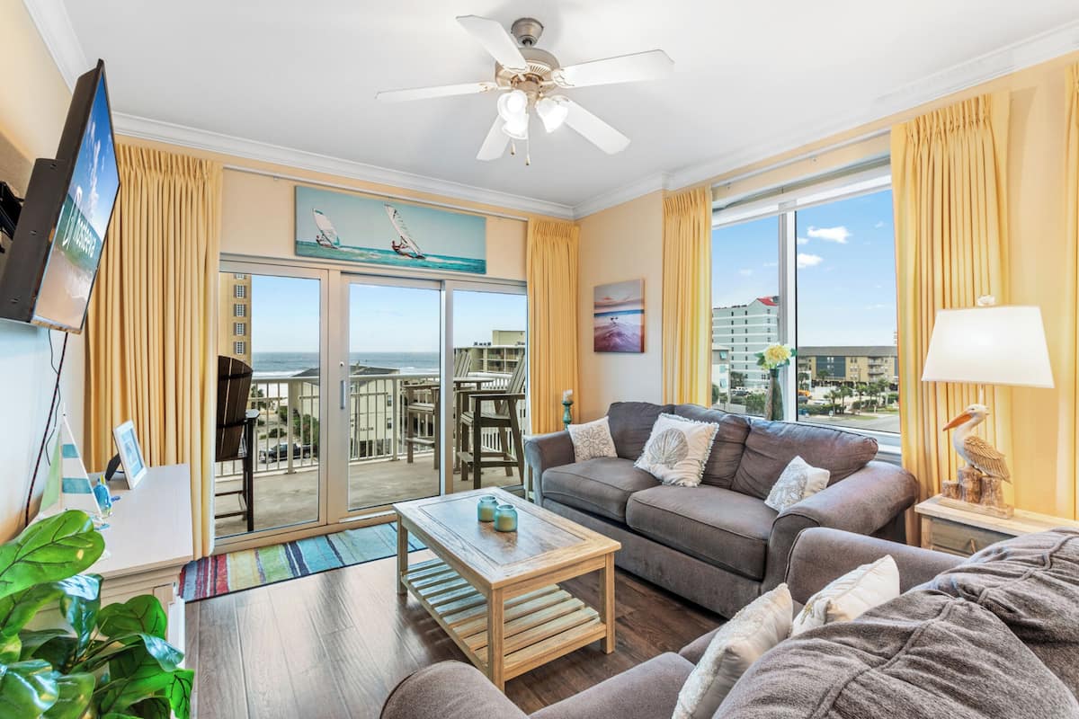 A spacious living room with a balcony, a ceiling fan, and a large window with curtains.