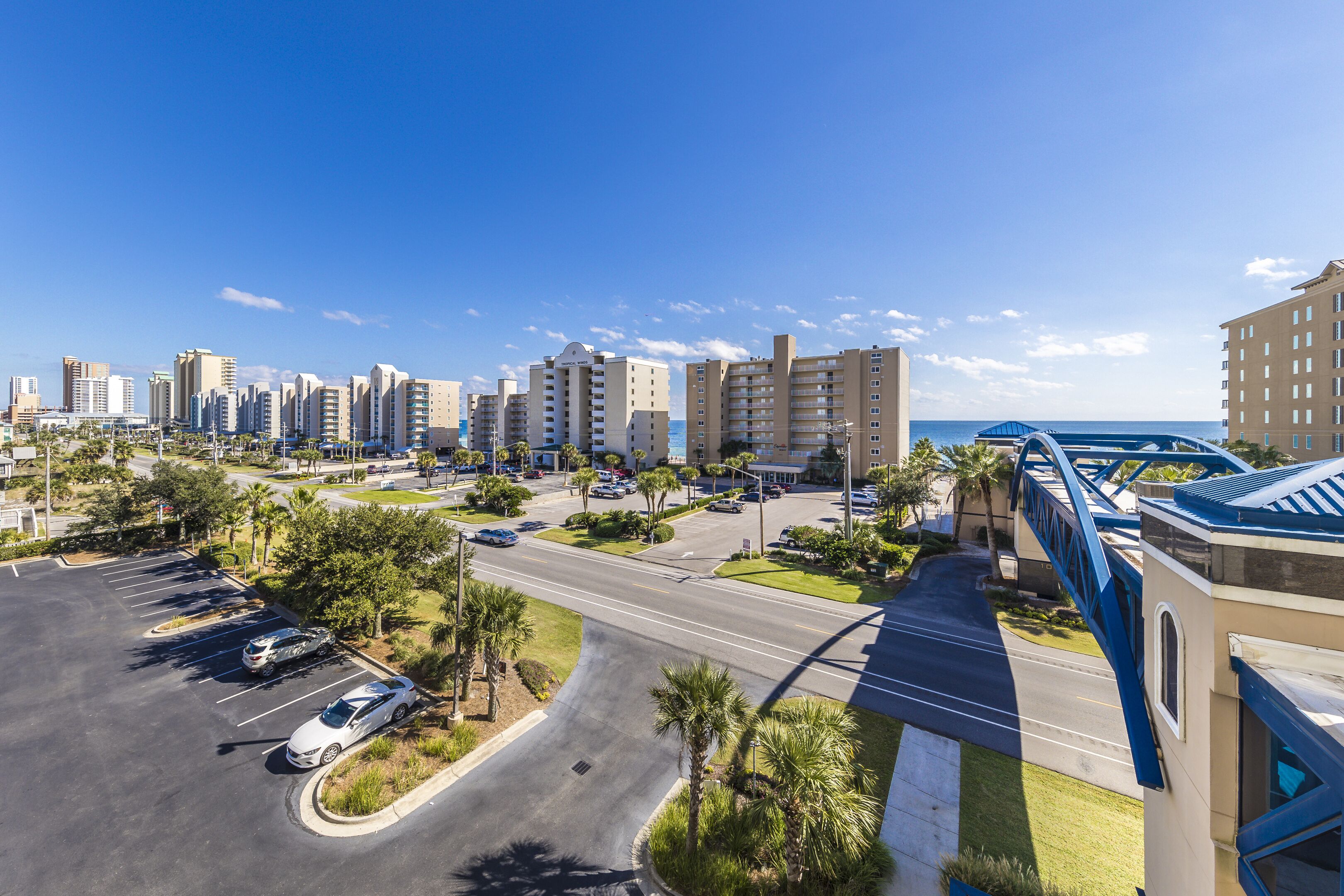 A high-rise hotel with multiple floors, a parking lot, and a view of the ocean.