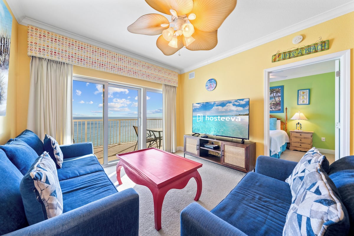 A living room with a TV, sofas, a red coffee table, and a balcony with a view.