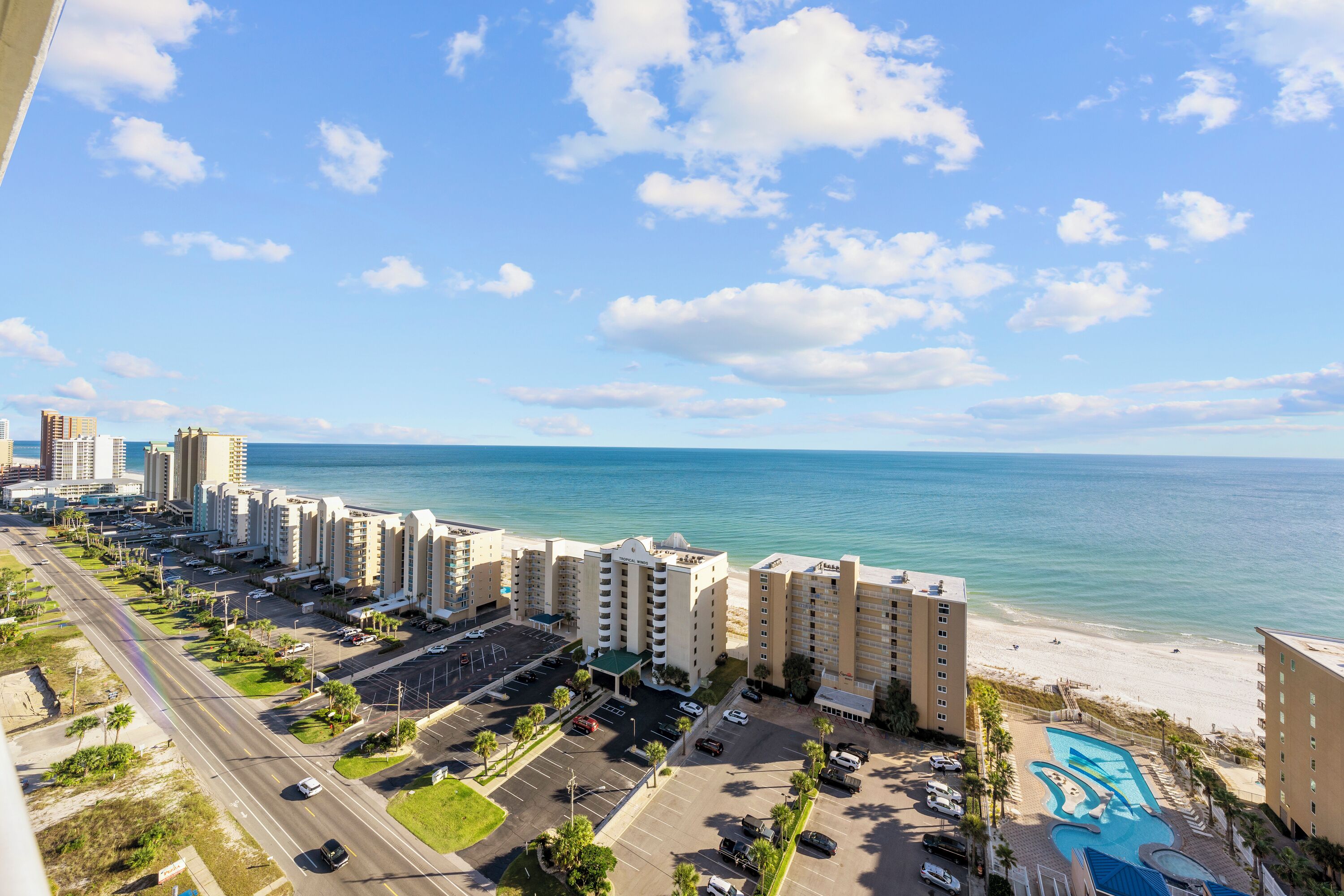 A beachfront hotel with multiple high-rise buildings, a parking lot, and a swimming pool.
