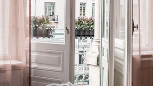 Una habitación con cama, ventana con vistas a edificios y balcones, y una puerta.