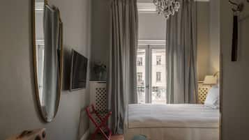 Habitación de hotel con cama, televisor, espejo y vista a edificios a través de la ventana.