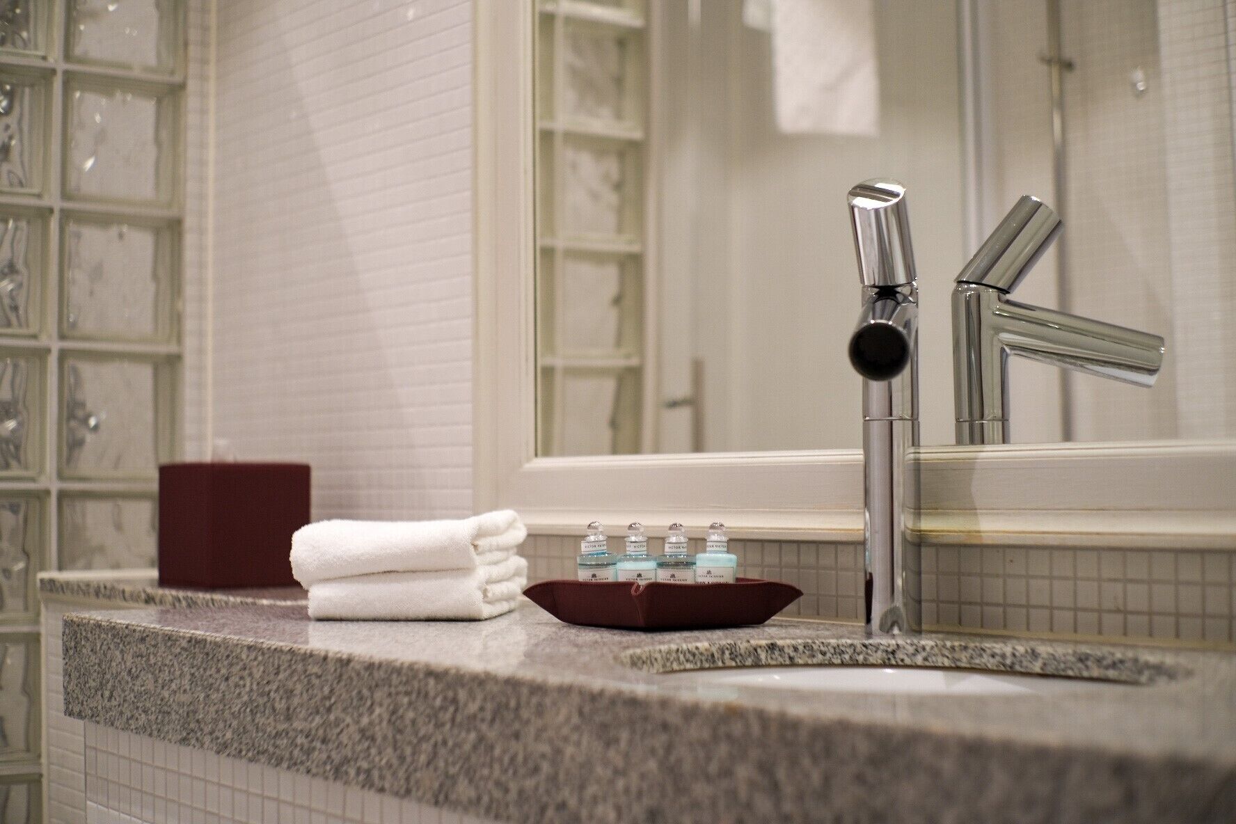Un baño con encimera de granito, un lavamanos con grifo moderno y un espejo que refleja la habitación.