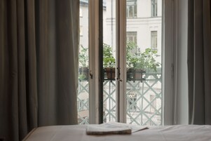Una habitación con una cama, una ventana con cortinas y vistas a un balcón con plantas en macetas.