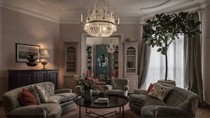 Una sala de estar con candelabro, sillones, una mesa de centro y una estantería.