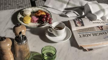 Una mesa de desayuno con un plato de comida, una taza de café, un periódico y un vaso verde.