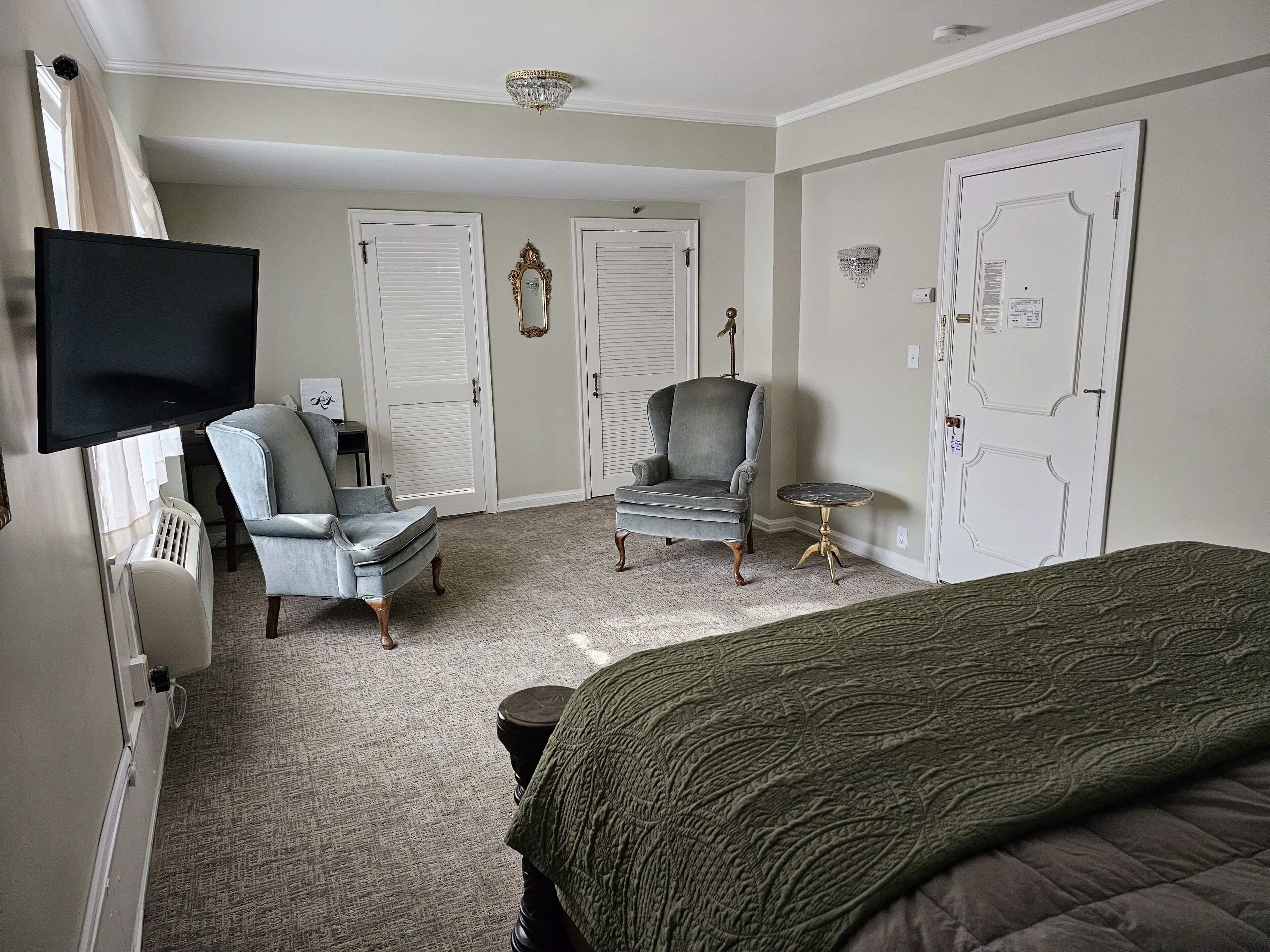 Une chambre à coucher comprenant un lit, deux fauteuils, une petite table, un téléviseur et une armoire.