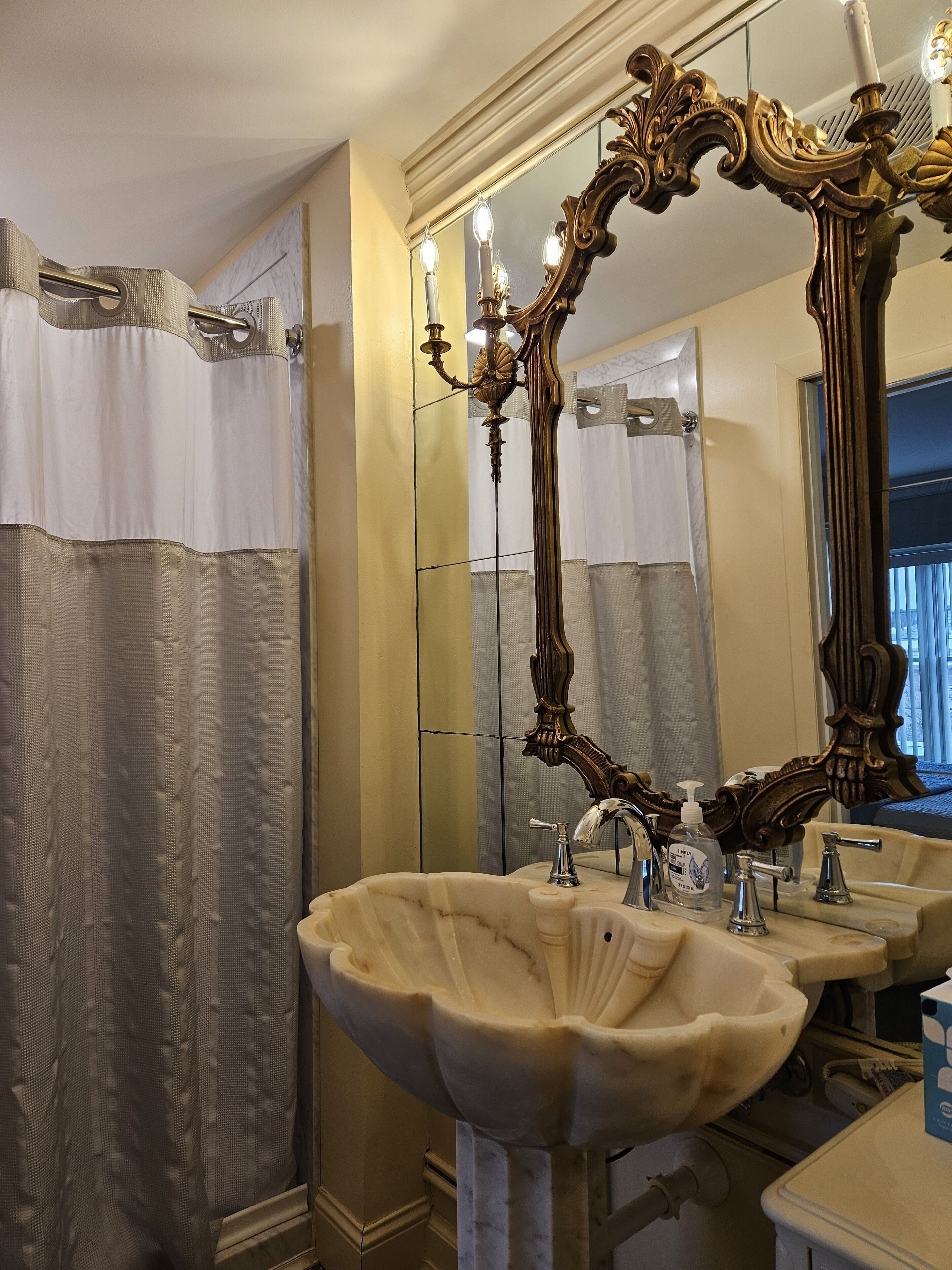 A bathroom with a large ornate mirror, a marble sink, and a shower curtain.
