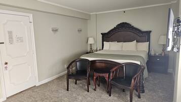 Quarto de hotel com uma cama grande, duas cadeiras, uma mesa de cabeceira e uma porta com fechadura de segurança.