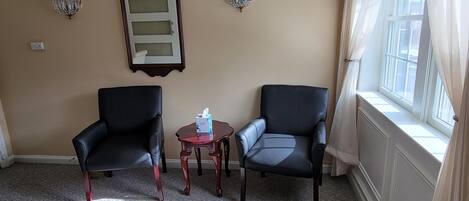 Una habitación con dos sillones de cuero negro, una mesita de madera con una caja de pañuelos, un espejo en la pared y dos apliques.