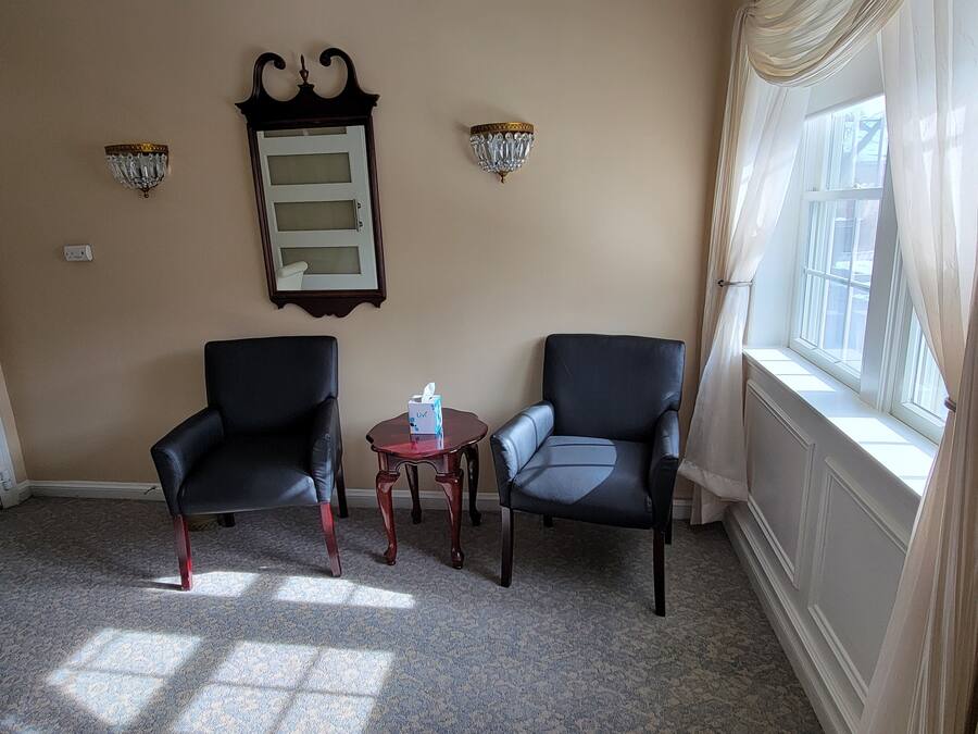 A room with two black leather chairs, a small wooden table with a tissue box, a wall-mounted mirror, and two wall sconces.