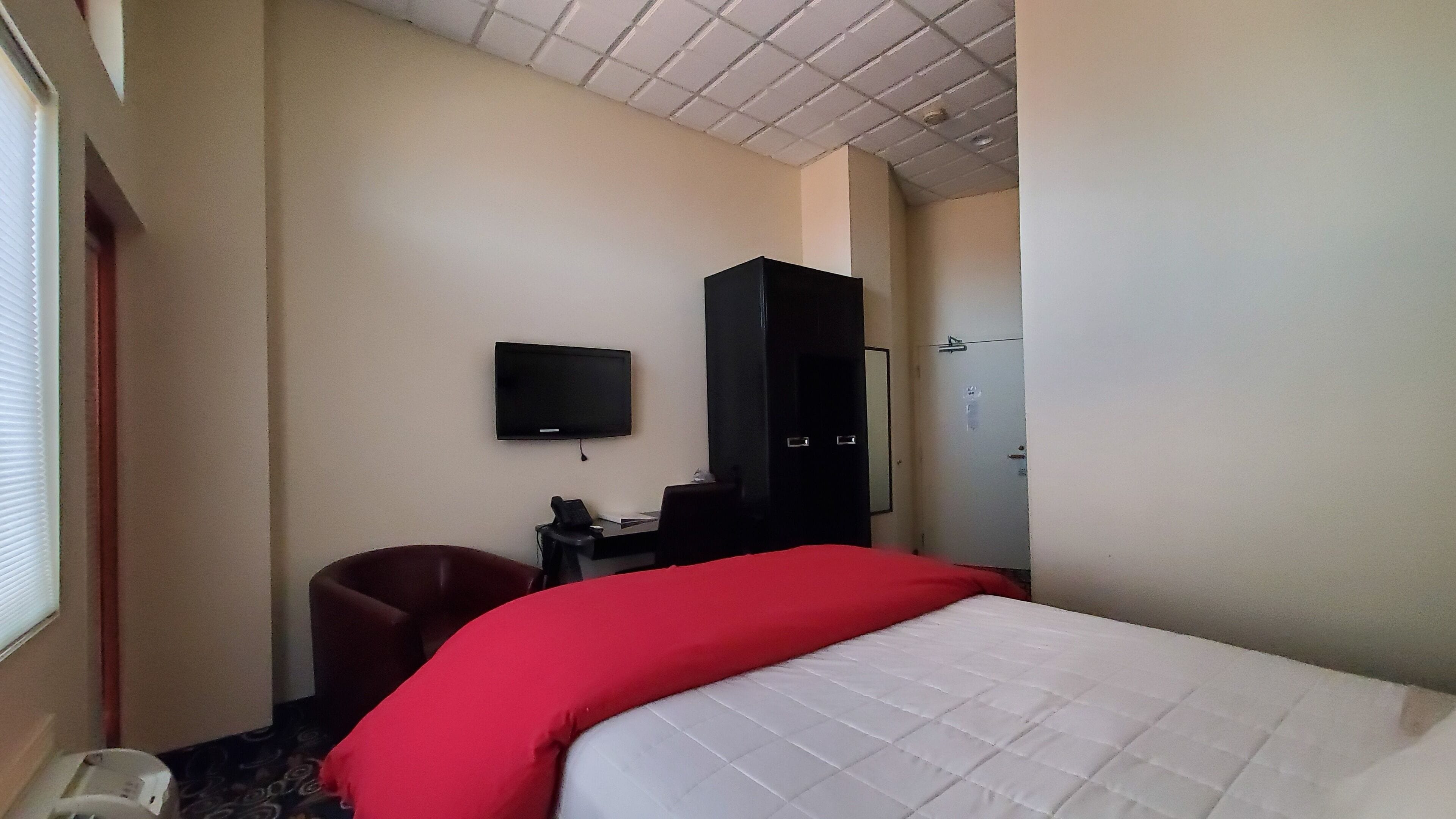 Una habitación de hotel con cama, escritorio con silla, televisor y armario.