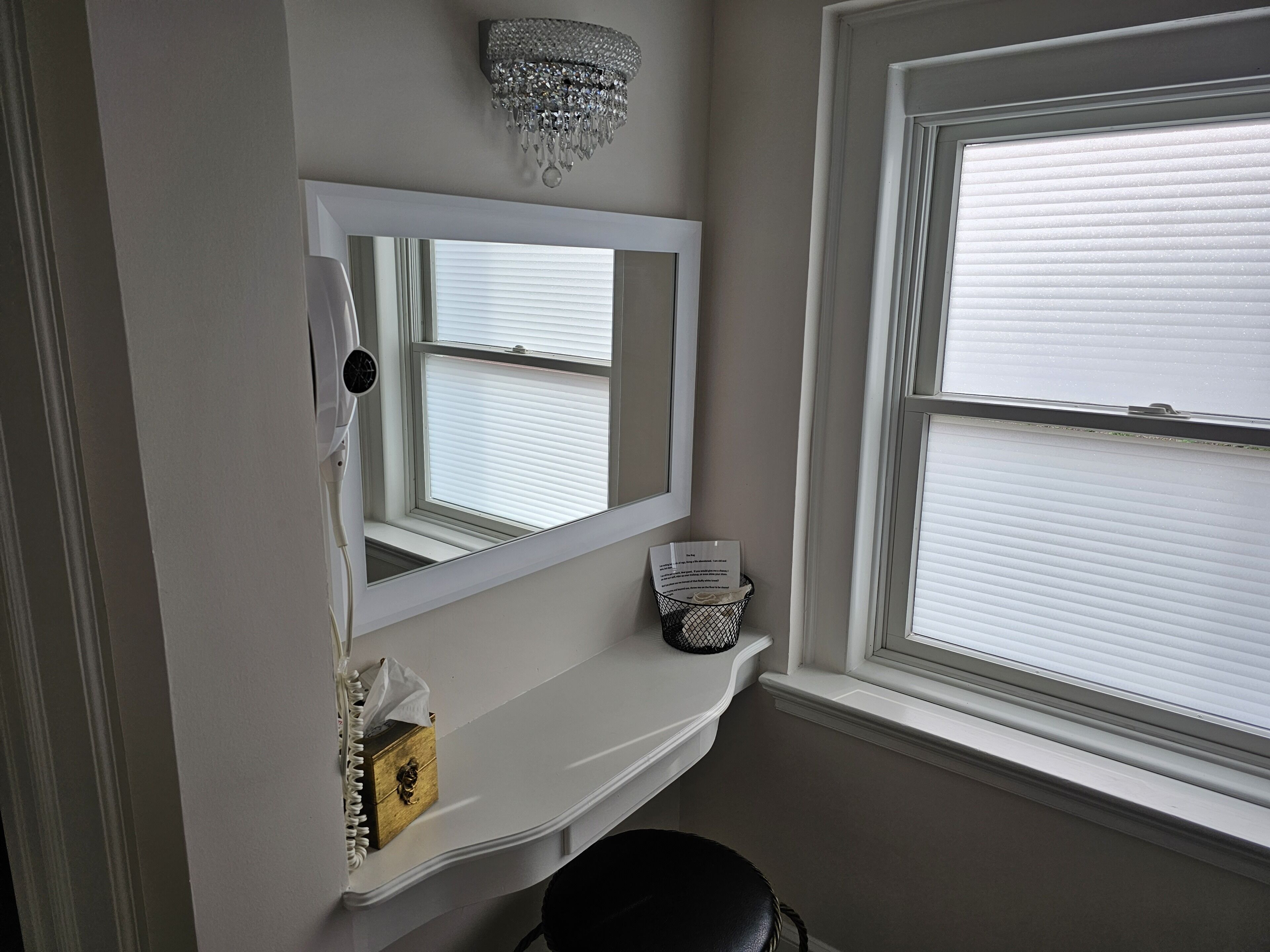 A bathroom with a vanity, a mirror, a chandelier, and a window with blinds.