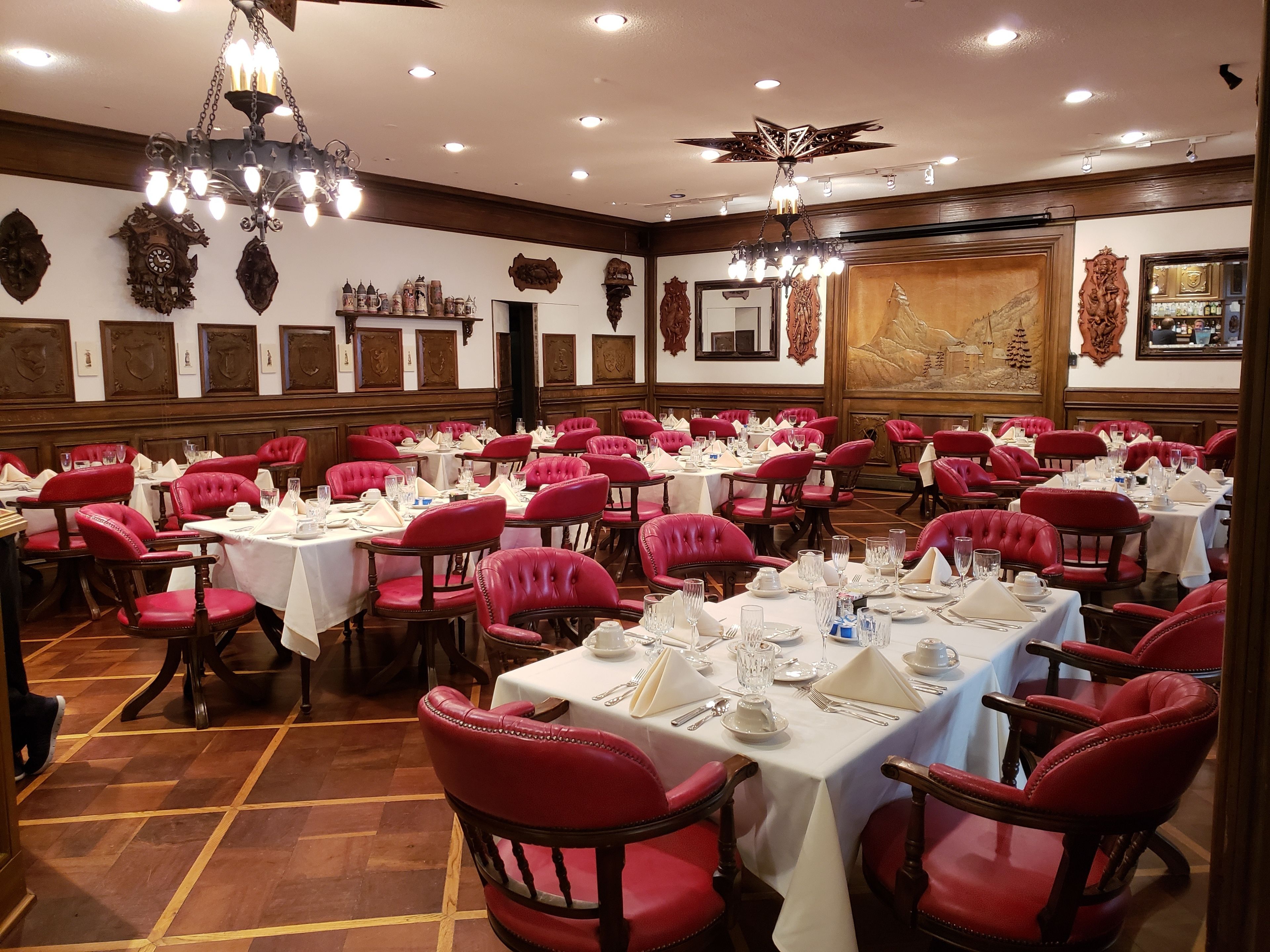 A banquet hall with red upholstered chairs, white tablecloths, and chandeliers.