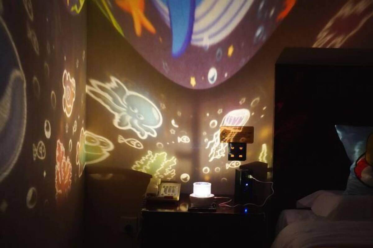 Una habitació amb un llit, una taula de nit amb una làmpada i una paret amb projecció de llum.