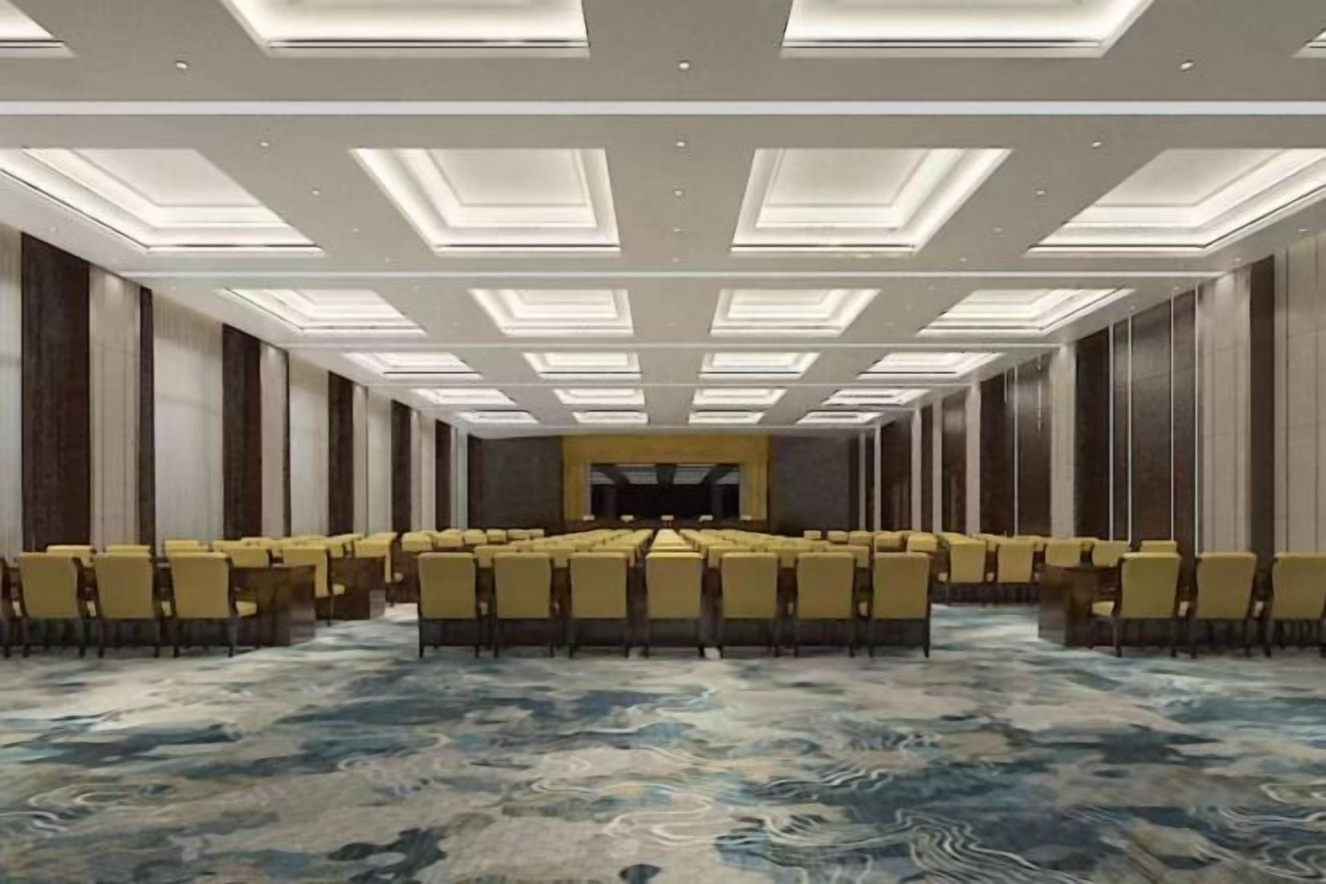 A conference room with a long table and chairs, a carpeted floor, and a high ceiling with recessed lighting.